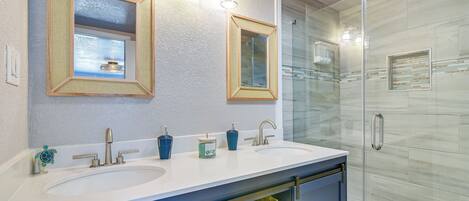 Une salle de bain avec deux lavabos, une douche à parois de verre et un grand miroir avec trois points lumineux.