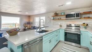 Una cucina con una grande isola, elettrodomestici in acciaio inossidabile, mobili color verde acqua e vista sull'esterno.