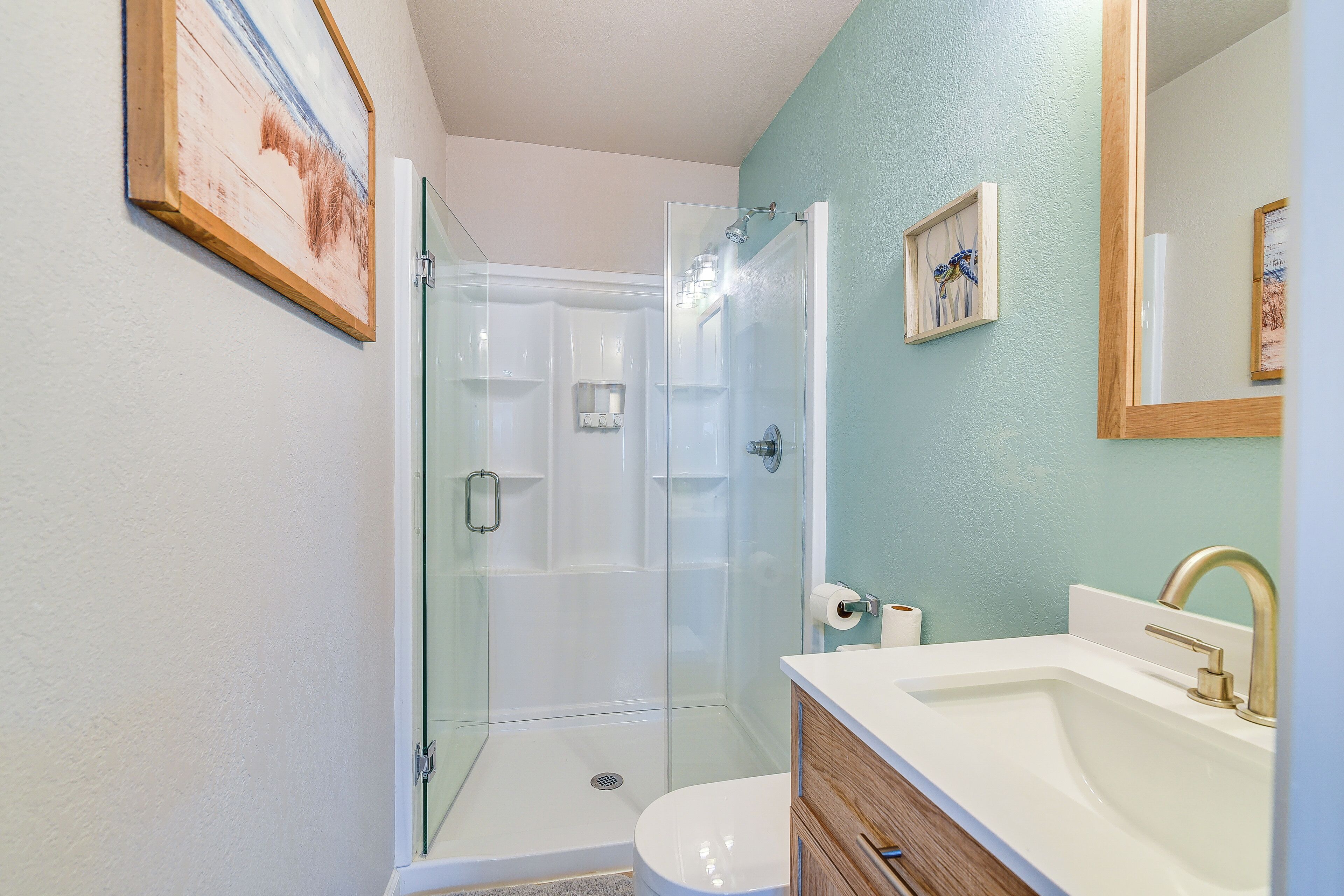 Un baño con ducha de vidrio, lavamanos blanco con grifo dorado y tocador de madera.