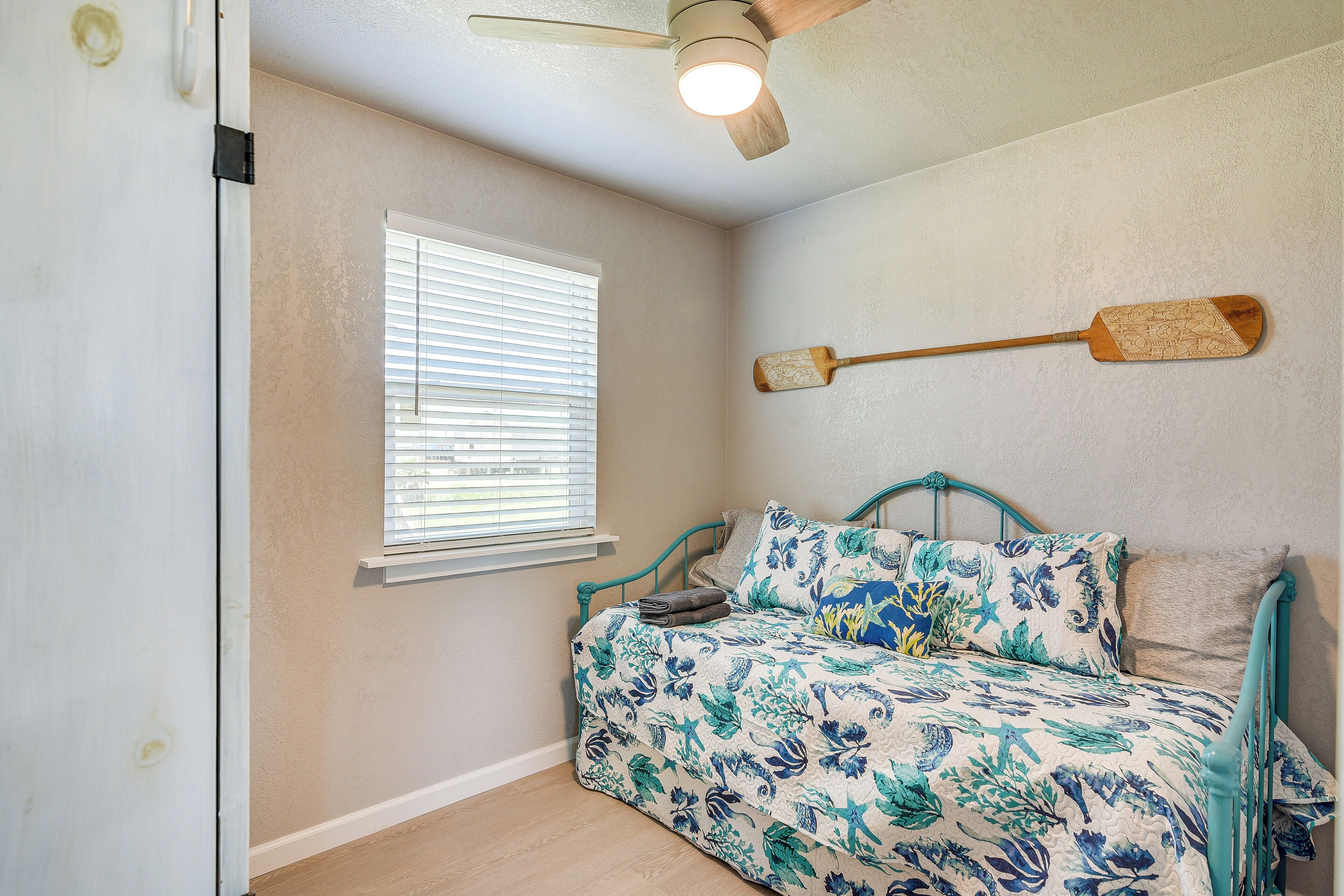 Un dormitorio con cama, ventilador de techo, ventana con persianas y una tabla de surf de remo montada en la pared.