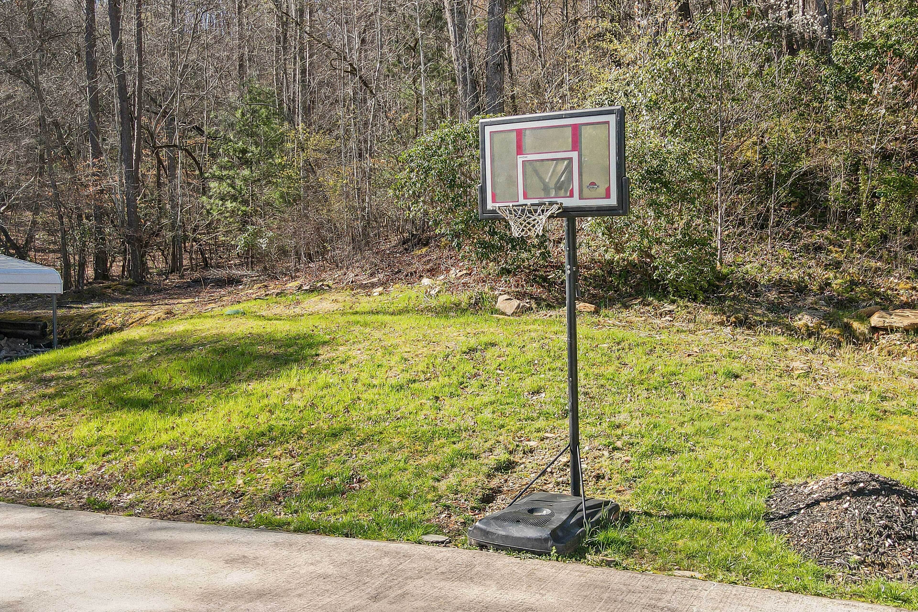 A basketball hoop in a grassy area with trees in the background.