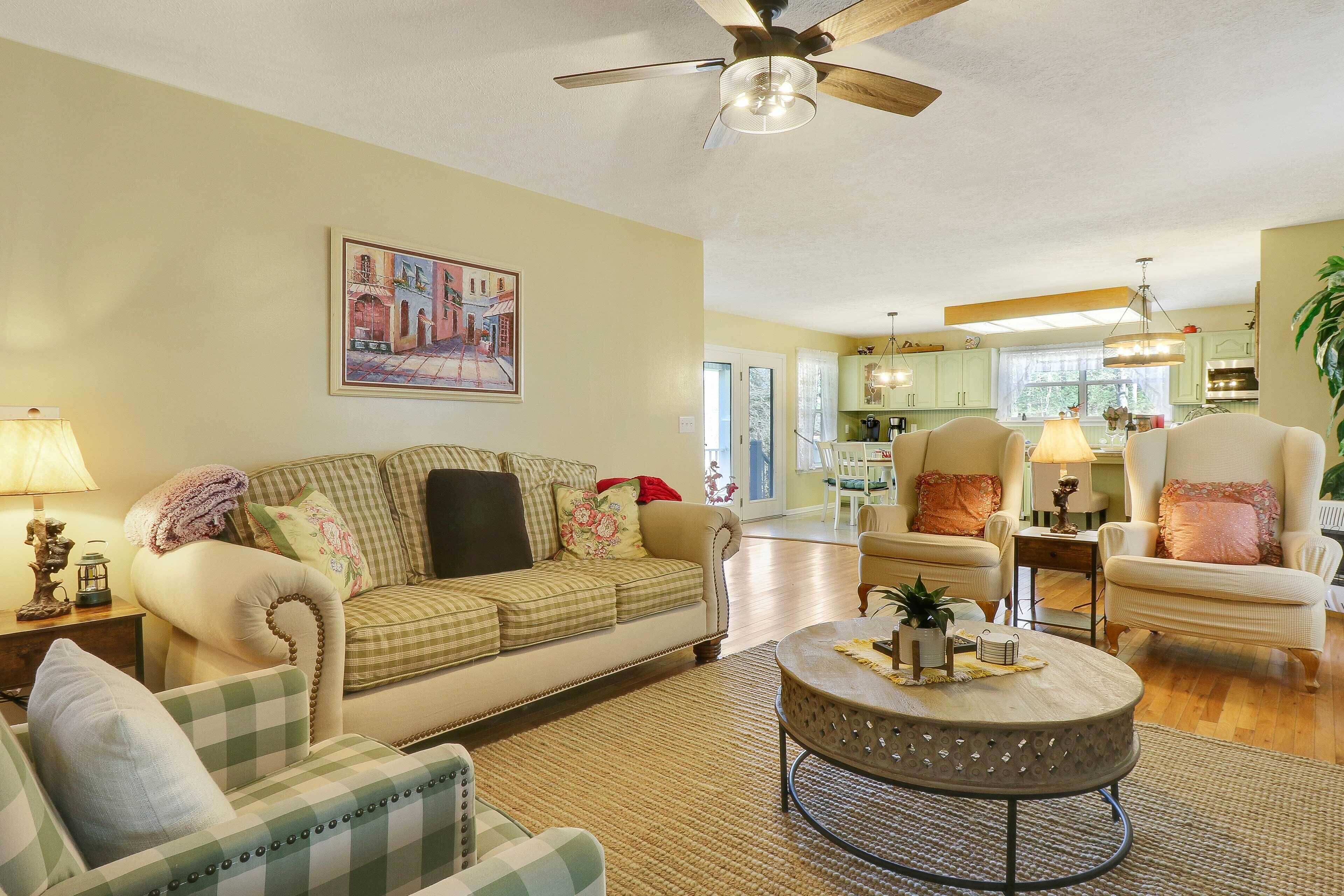 A living room with a sofa, armchairs, a coffee table, and a ceiling fan.