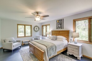 A bedroom with a bed, a nightstand, a chair, a ceiling fan, and large windows. - Secluded Wautoma Home w/ Fire Pit! (Wautoma)