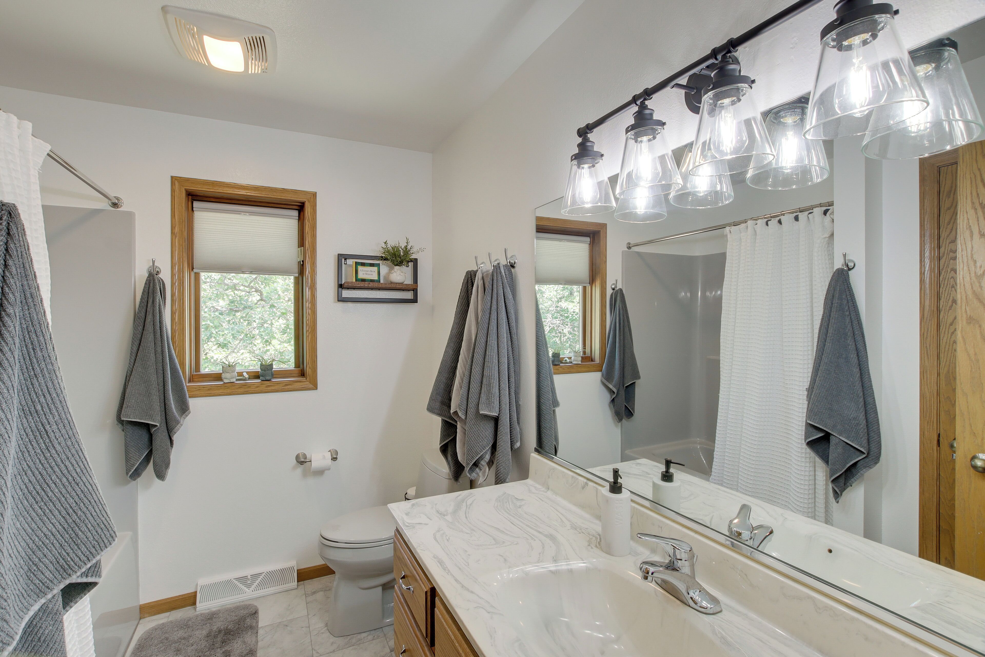 A bathroom with a white toilet, a sink with a marble countertop, a large mirror, and multiple towel racks.