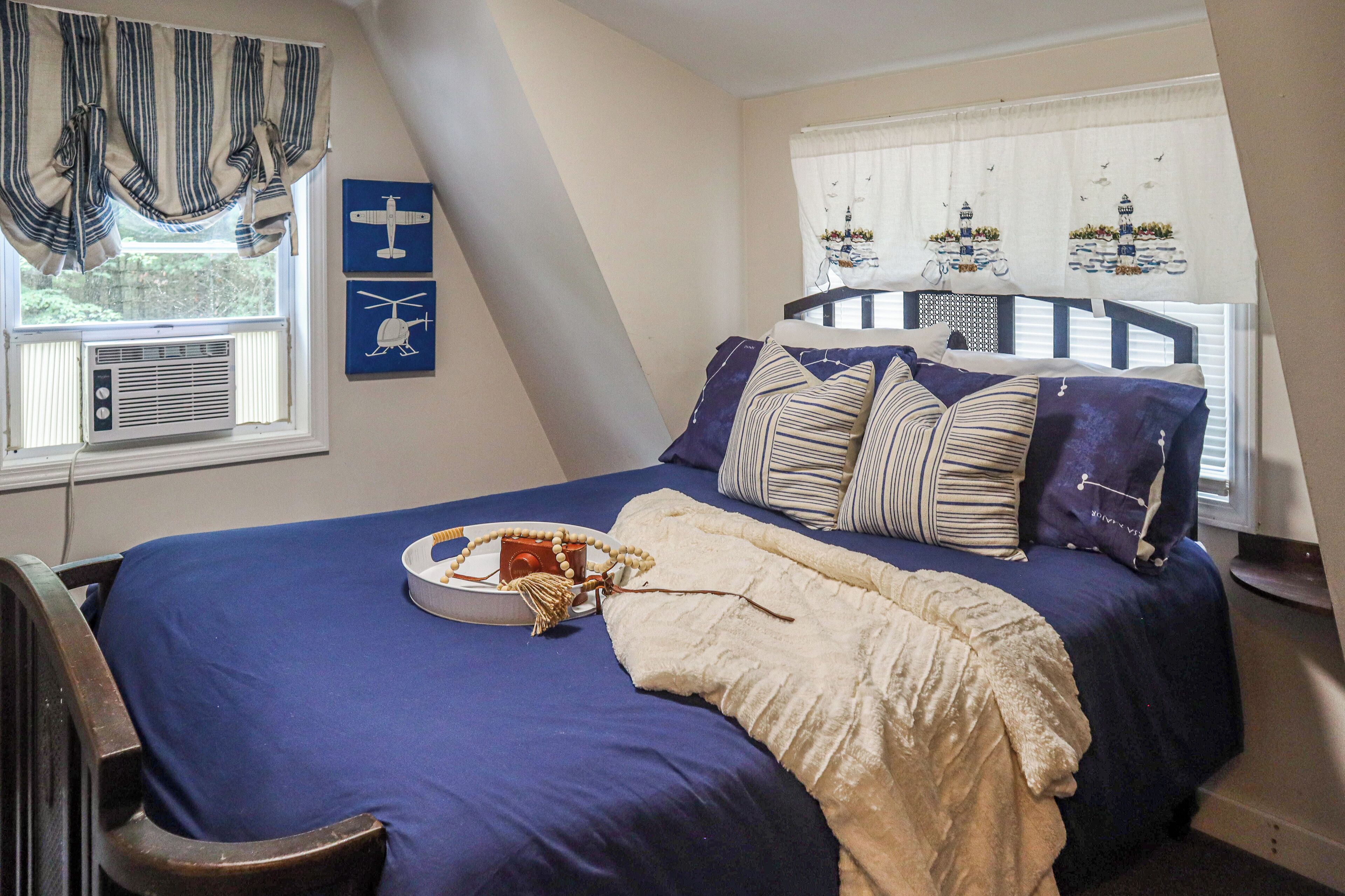 A bedroom with a bed, a window with curtains, an air conditioning unit, and wall decorations.