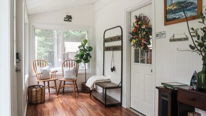 A cozy room with a wooden floor, a bench, two chairs, a small table, a potted plant, a painting, and a door with a sign. - Huguenot Retreat w/ Screened Porch & Lake Access! (Huguenot)