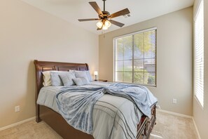 Ein Schlafzimmer mit einem Bett, einem Deckenventilator, einem Fenster mit Jalousien und einem Teppichboden.