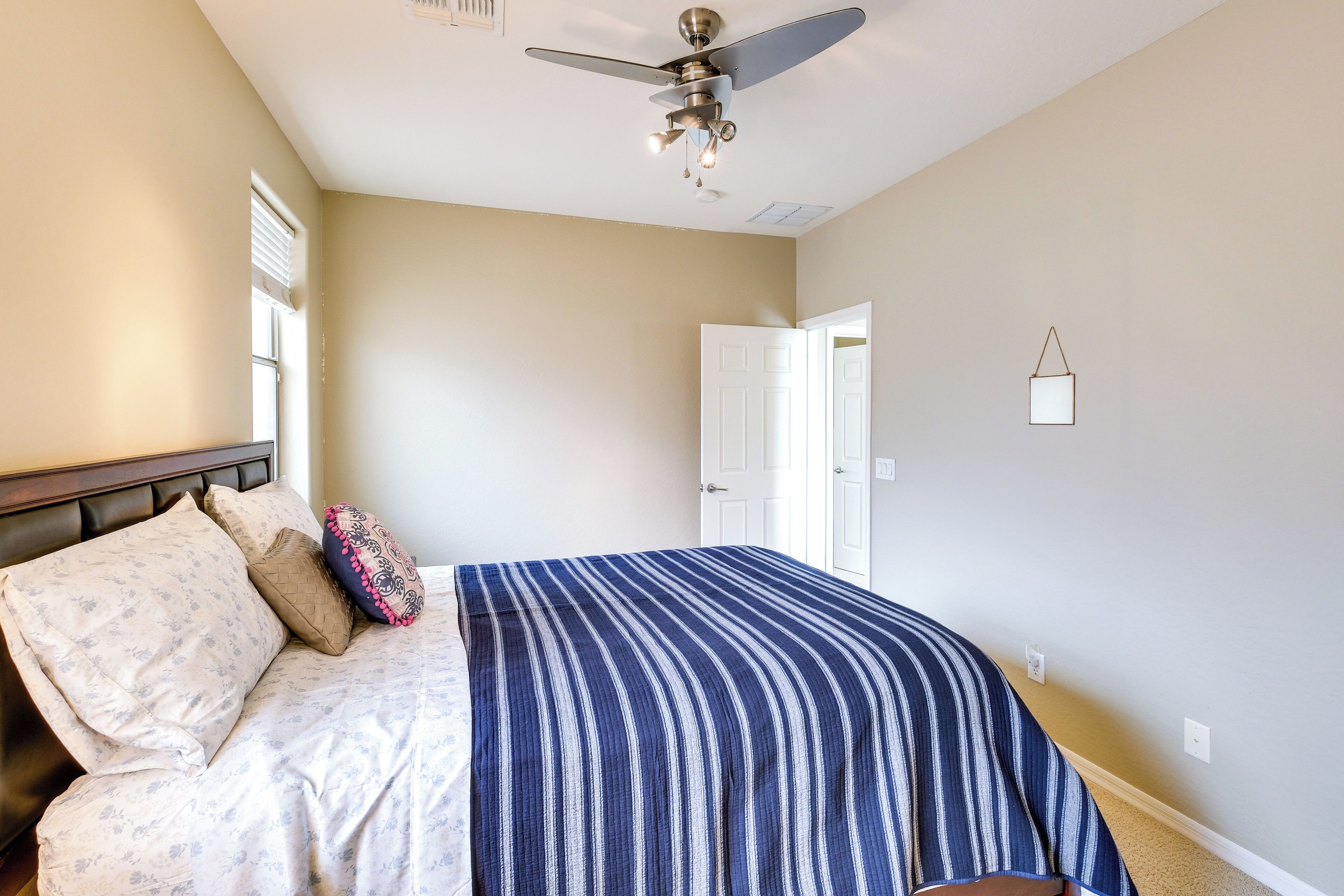 A bedroom with a bed, a ceiling fan, a window, and a door.