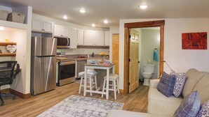 A compact kitchen with white cabinets, a stainless steel refrigerator, and a dining area with stools. - Southern Colorado Rental: 10 Mi to Mesa Verde (Cortez)