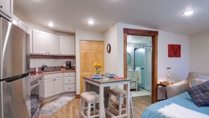 A compact kitchen with white cabinets, a dining table with two stools, and a blue bed with a white throw. - Southern Colorado Rental: 10 Mi to Mesa Verde (Cortez)