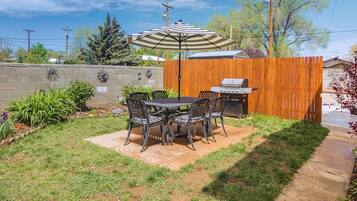 A backyard with a patio table and chairs, a grill, and a wooden fence.