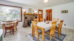 A dining area with a wooden table and chairs, a stone fireplace, and a ceiling fan. - Lakefront Minnesota Escape w/ Fire Pit & Boat Dock (Emily)