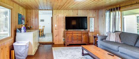 A wooden-paneled living room with a sofa, a television, and a dining area with a small table and chairs.
