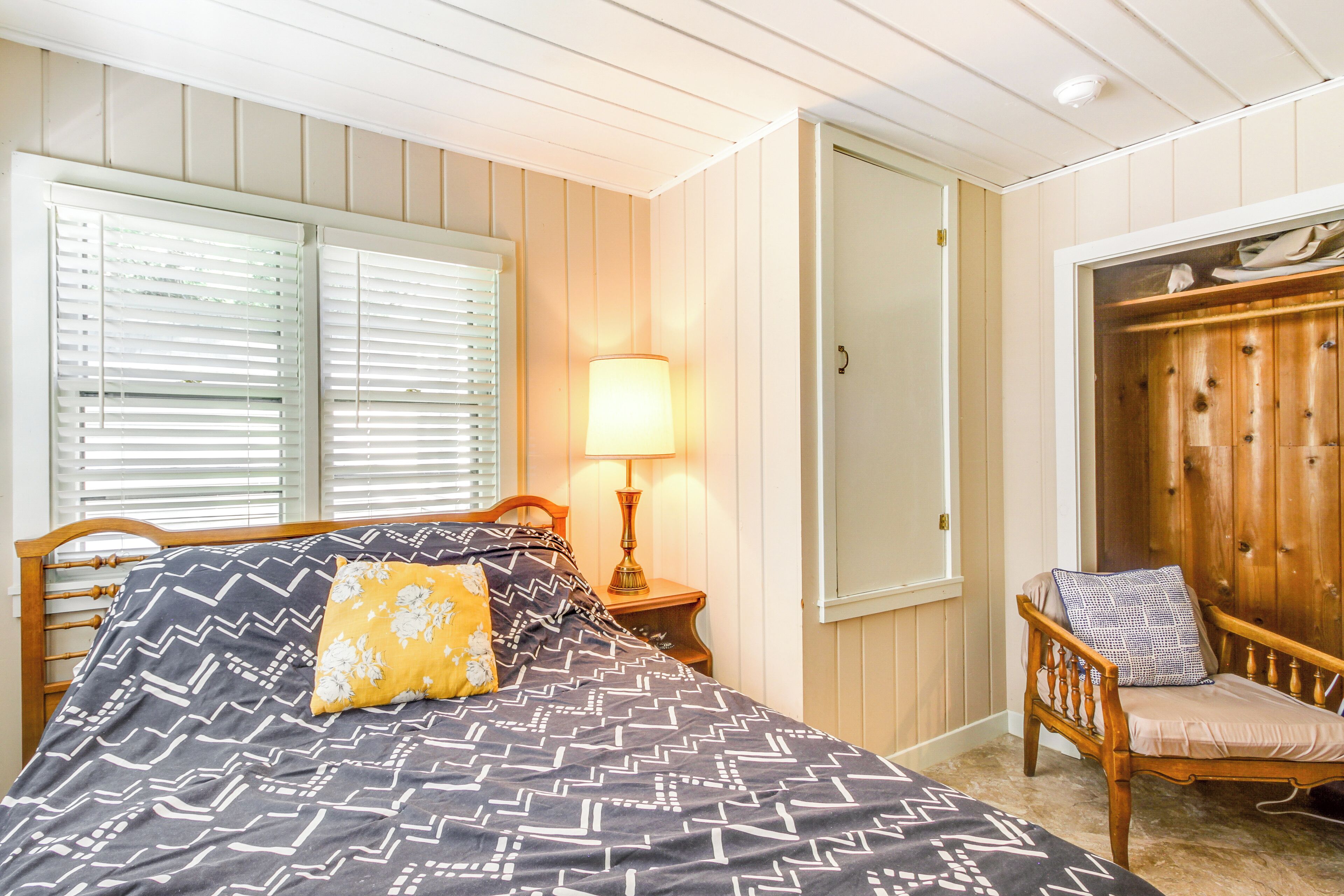 A bedroom with a bed, a nightstand with a lamp, a wooden chair, and a wardrobe.