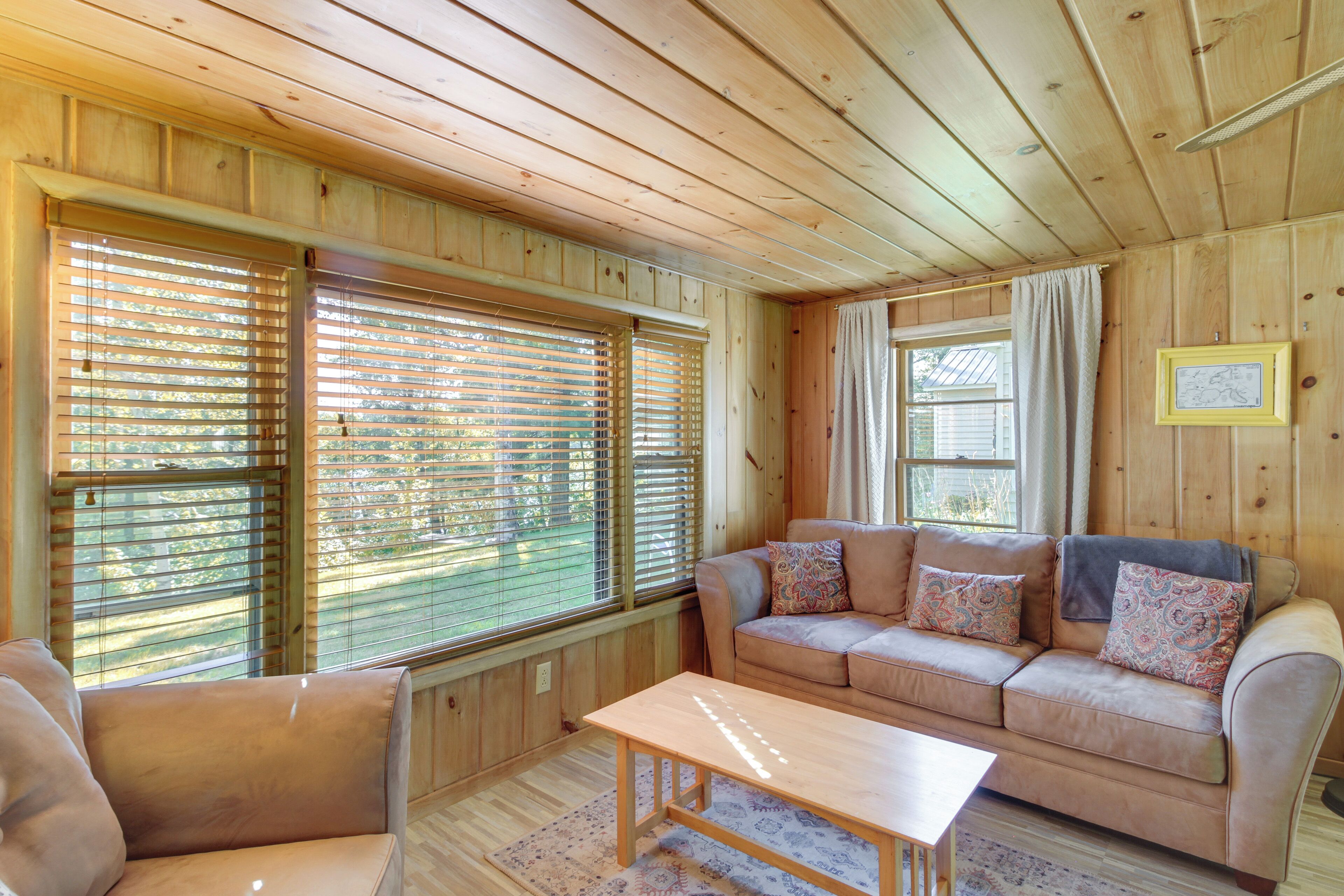 A wooden-paneled room with a beige sofa, a wooden table, and large windows with blinds.
