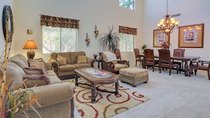 A spacious living room with a large sofa, a coffee table, and a dining area with a chandelier. - Spacious Maricopa Home Rental w/ Pool & Hot Tub! (Maricopa)