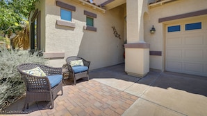 A house with a patio area featuring wicker furniture and a garage. - Spacious Maricopa Home Rental w/ Pool & Hot Tub! (Maricopa)