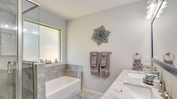 A modern bathroom with a glass shower enclosure, a bathtub, two sinks, and a decorative wall piece.