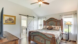 A bedroom with a wooden bed, a ceiling fan, a TV, and a window with curtains. - Inviting Granbury Home w/ Fire Pit: 3 Mi to Lake! (Granbury)