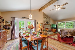 A spacious dining area with a wooden table set for four, a stone fireplace, and a view of the outdoors through large windows. - Pet-friendly Retreat w/ Mtn Views in Sylva! (Sylva)