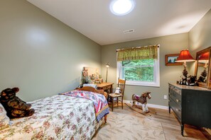 Une chambre à coucher comprenant un lit, un bureau, une chaise, une commode et une fenêtre donnant sur un paysage verdoyant.