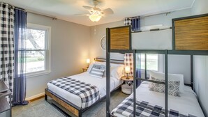 A bedroom with two beds, a ceiling fan, a window with curtains, and a bedside table with a lamp. - Sturgeon Bay Home ~ 6 Mi to Potawatomi State Park (Sturgeon Bay)