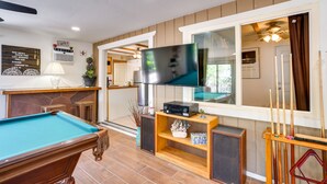 Een biljart, een televisie en een biljarthouder in een kamer met een stenen openhaard, houten planken en een grote spiegel.