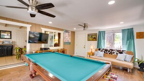 Een pooltafel in een ruimte met een bank, een plafondventilator en een televisie.