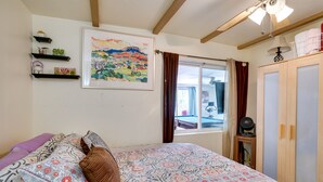 Een slaapkamer met een bed, een raam met gordijnen, een plafondventilator en een houten garderobe.
