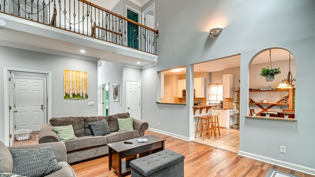 A spacious living room with a high ceiling, a wooden floor, a grey sofa, a coffee table, and a staircase leading to an upper level. - North Carolina Getaway on Pinehurst Golf Course! (Pinehurst)