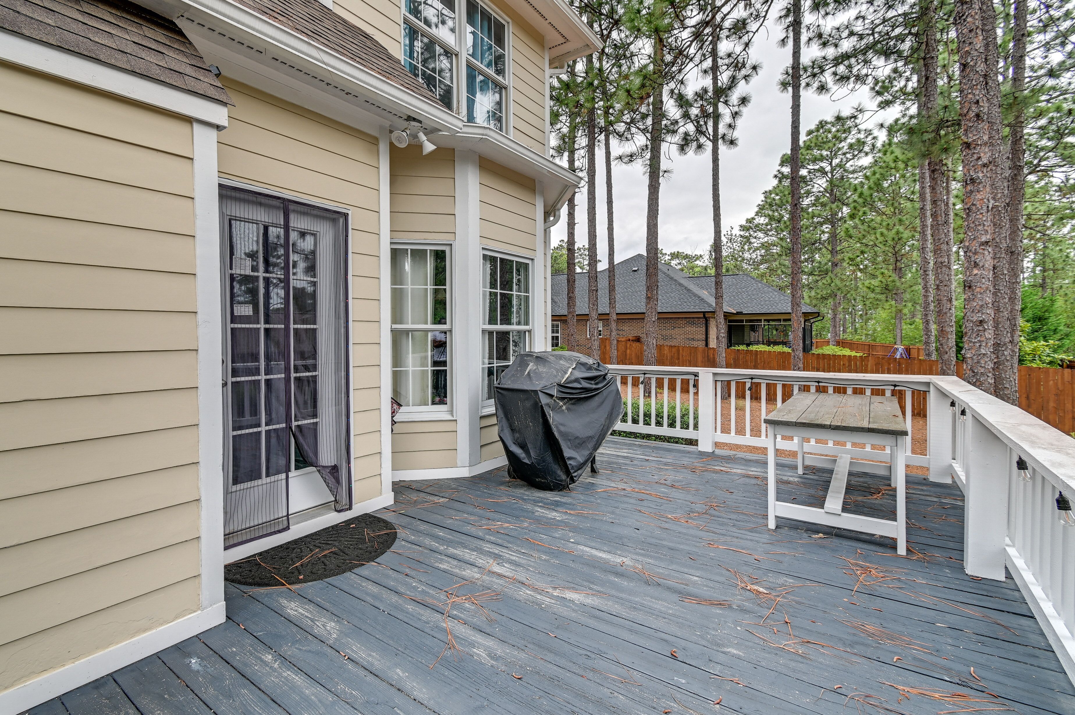 A covered deck with a table and chairs, a covered grill, and a wooden fence.