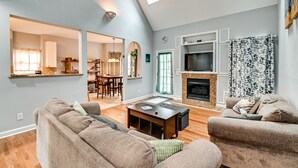 A spacious living room with a fireplace, a dining area, and a kitchen visible through an archway. - North Carolina Getaway on Pinehurst Golf Course! (Pinehurst)