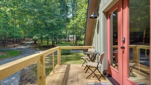 A wooden deck with a glass door leading to a room, a small table with chairs, and a view of a forested area. - Dog-friendly Mills River Retreat Near Hiking! (Mills River)