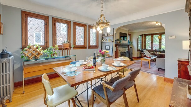 Un coin repas avec une table en bois, dressée pour quatre personnes, entourée de chaises, et un lustre au-dessus.