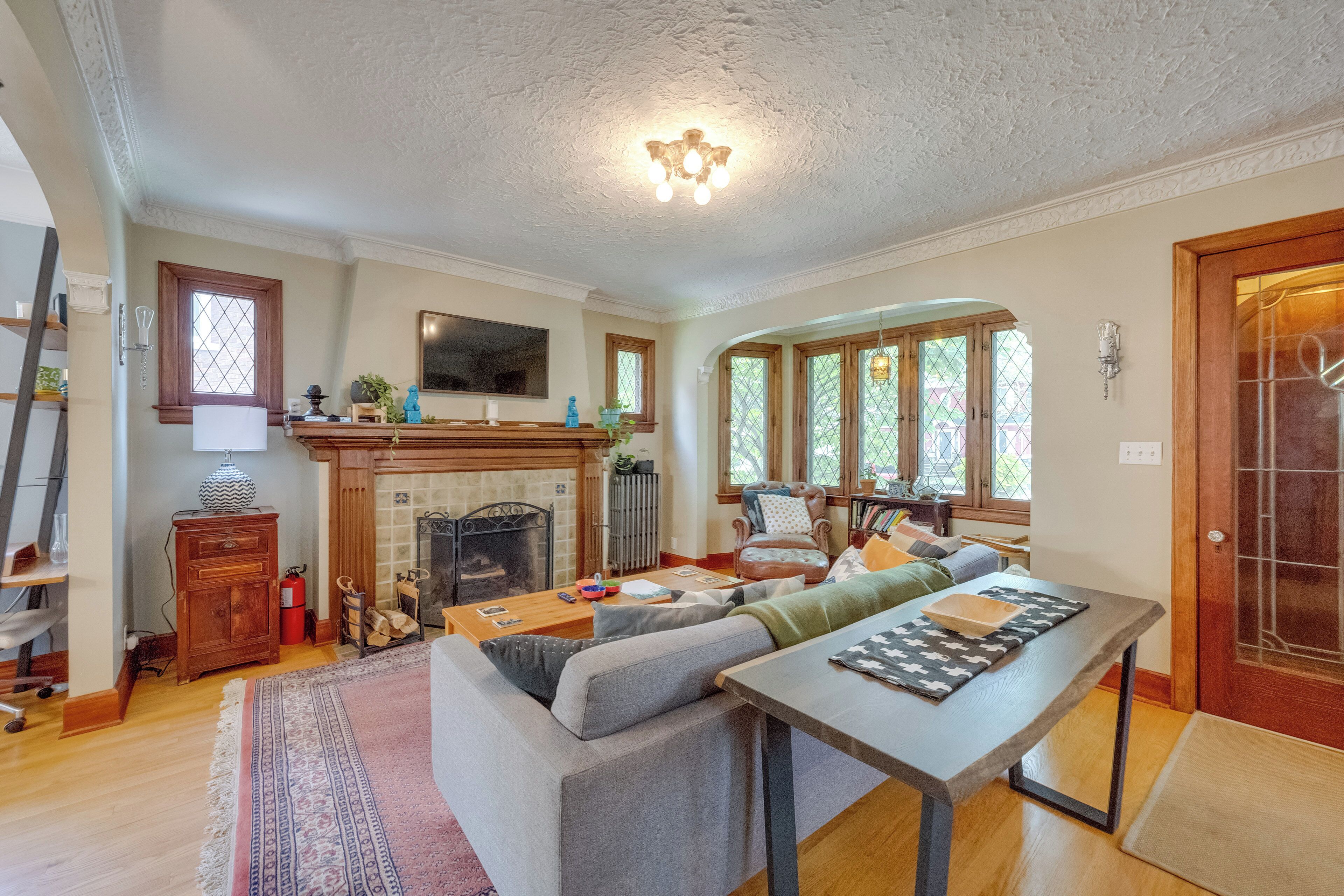 A cozy living room with a fireplace, a large sofa, a dining table, and a wooden floor.