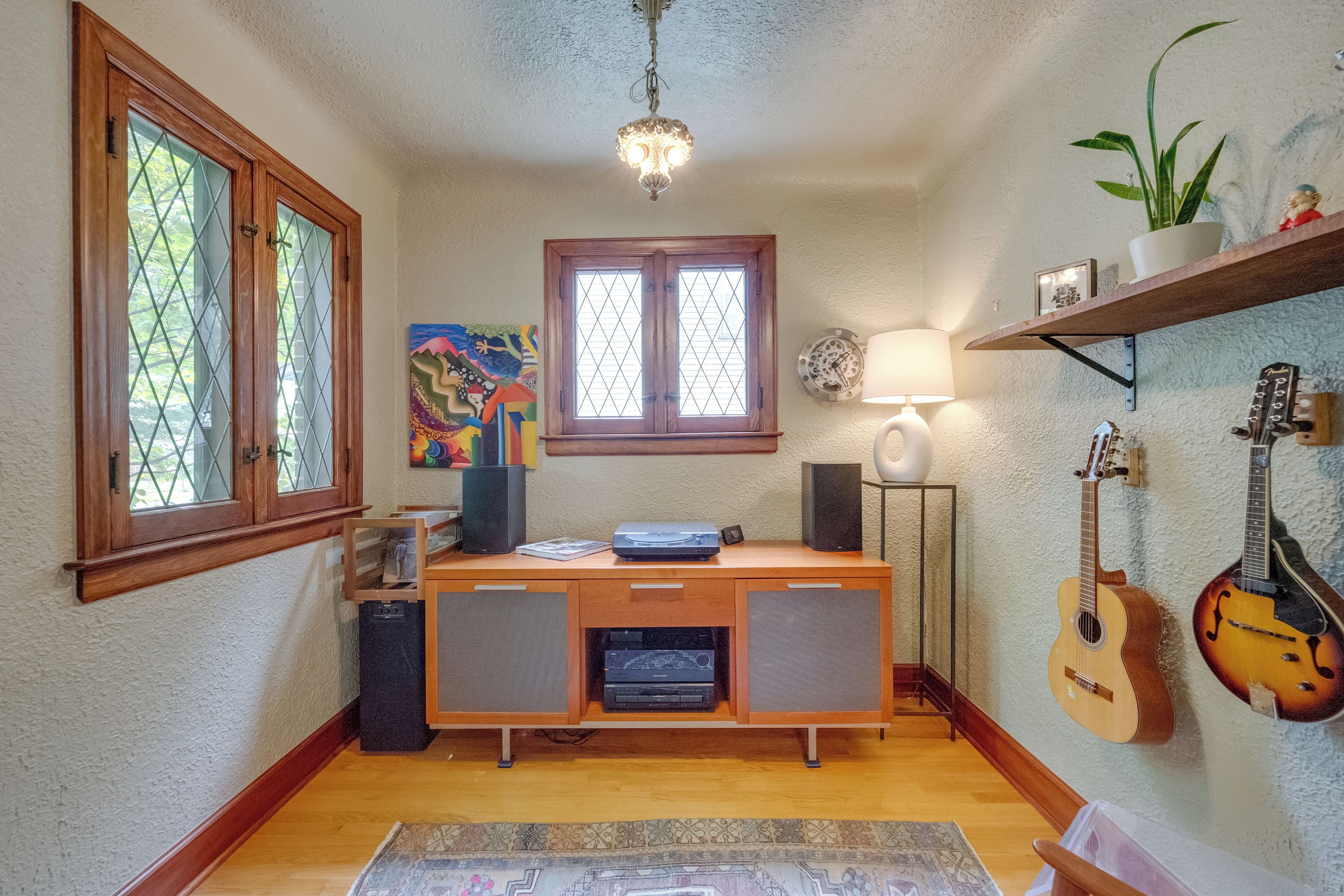 Une pièce avec un bureau en bois, des haut-parleurs, une guitare, une plante et un tableau.