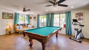 A room with a pool table, ceiling fans, a sofa, a treadmill, and large windows with curtains. - Green Valley Vacation Rental Apt w/ Patio & Grill! (Green Valley)