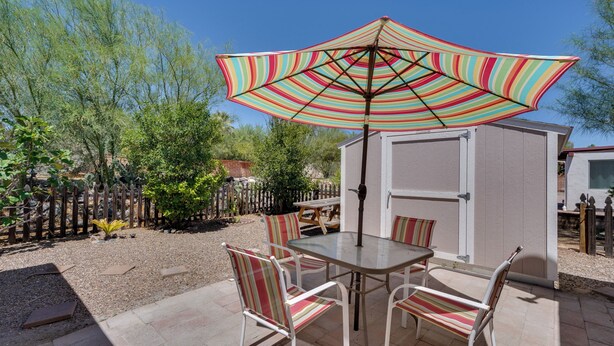 A patio with a table and chairs, a striped umbrella, and a small shed. - Green Valley Vacation Rental Apt w/ Patio & Grill! (Green Valley)