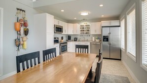 A modern kitchen with white cabinets, a stainless steel refrigerator, and a wooden dining table. - Vacation Rental House Situated on Chesapeake Bay (Ridge)