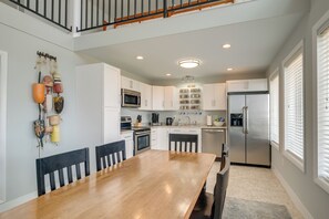 A modern kitchen with white cabinets, a stainless steel refrigerator, and a wooden dining table. - Vacation Rental House Situated on Chesapeake Bay (Ridge)