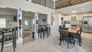 A spacious kitchen with modern appliances, a dining area with wooden furniture, and a second-floor balcony with a railing. - Vacation Rental House Situated on Chesapeake Bay (Ridge)
