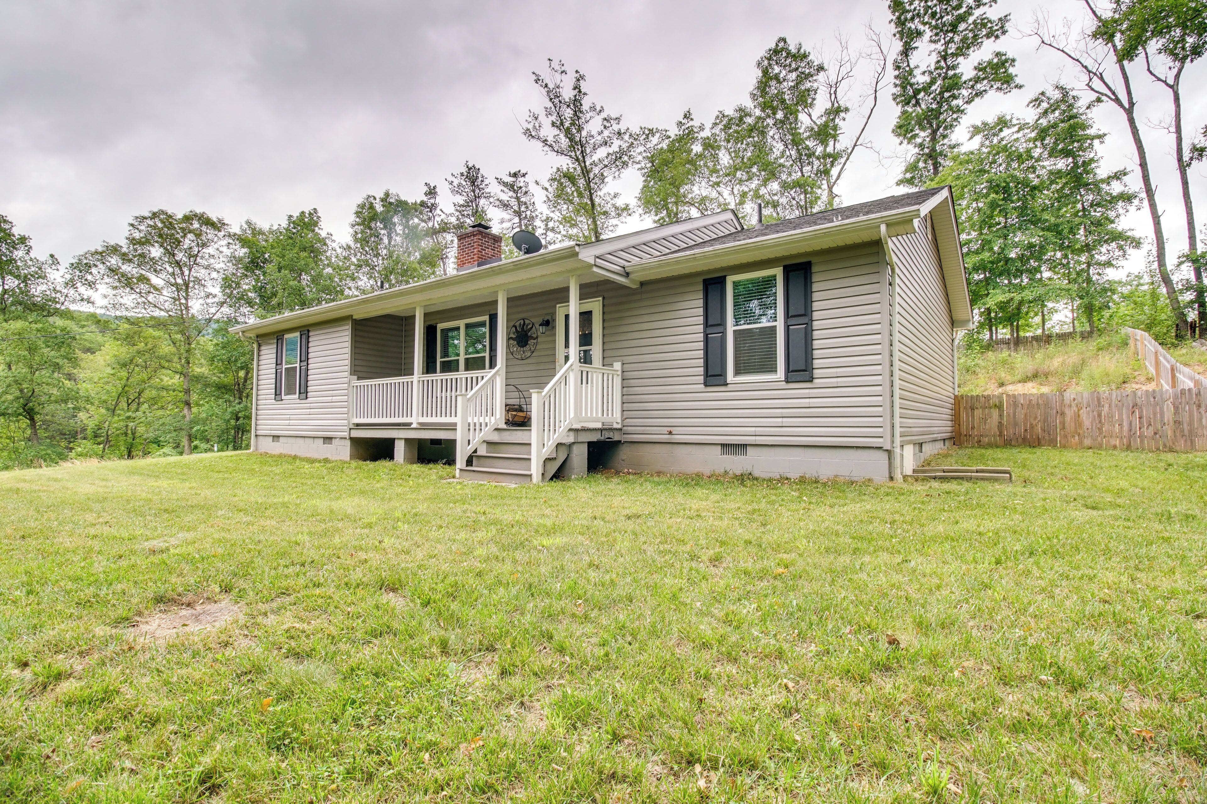 A single-story house with a front porch, a chimney, and a fenced yard.
