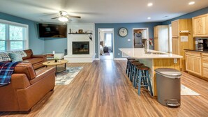 A modern living room with a brown leather sofa, a coffee table, and a fireplace. The kitchen features wooden cabinets, a sink, and a countertop. - Cozy Home in Star Tannery w/ Private Backyard! (Strasburg)