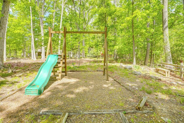 Un parque infantil con un tobogán y una estructura de madera para escalar, ubicado en un área boscosa.