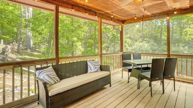 A covered outdoor deck with a sofa, chairs, and a table, overlooking a forested area. - Mcgaheysville Home w/ Screened Porch & Gas Grill! (McGaheysville)