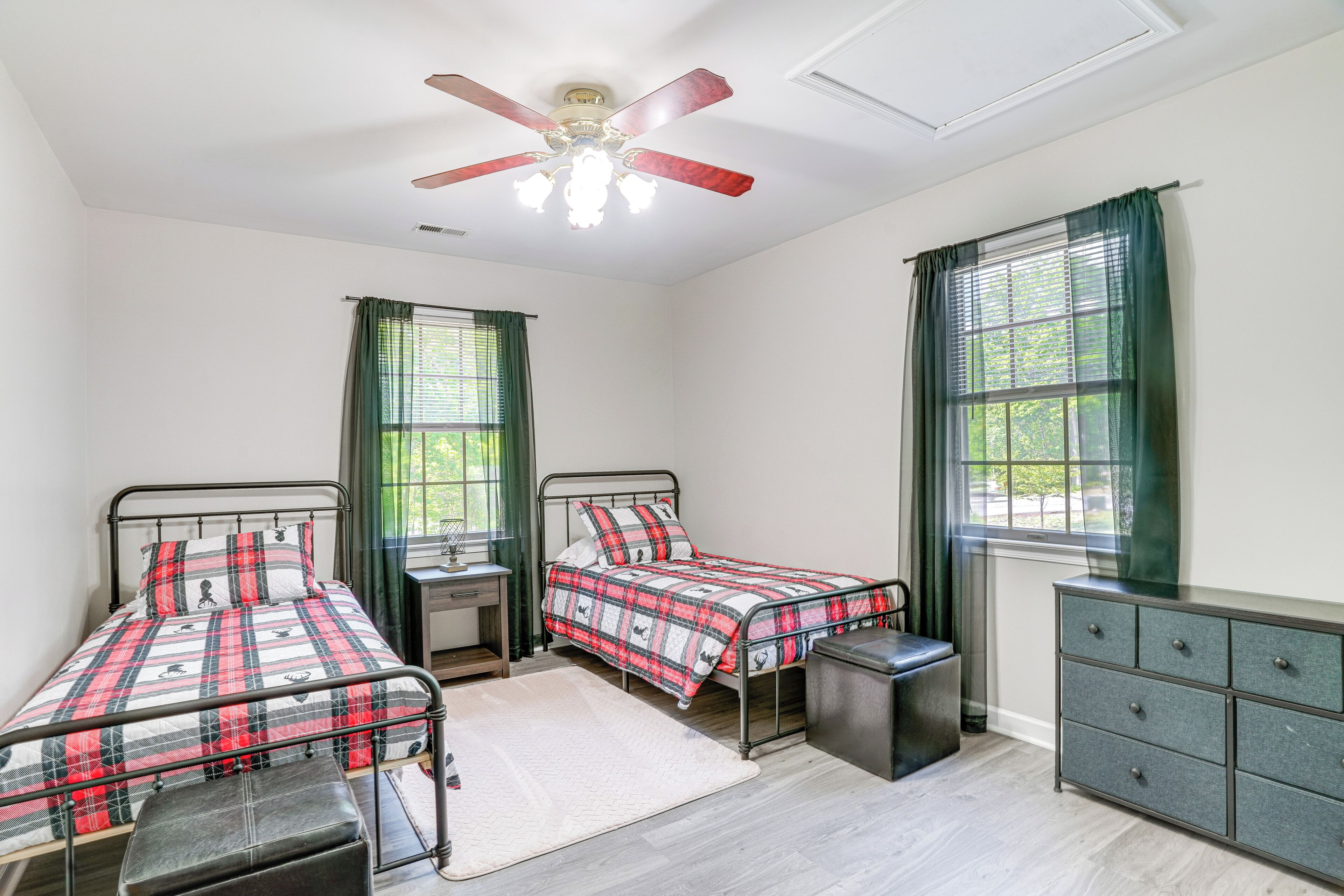 A bedroom with two beds, a ceiling fan, a dresser, and a window with curtains.