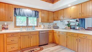 A kitchen with wooden cabinets, a dishwasher, a window with a curtain, and a rug on the floor. - Mcgaheysville Home w/ Screened Porch & Gas Grill! (McGaheysville)