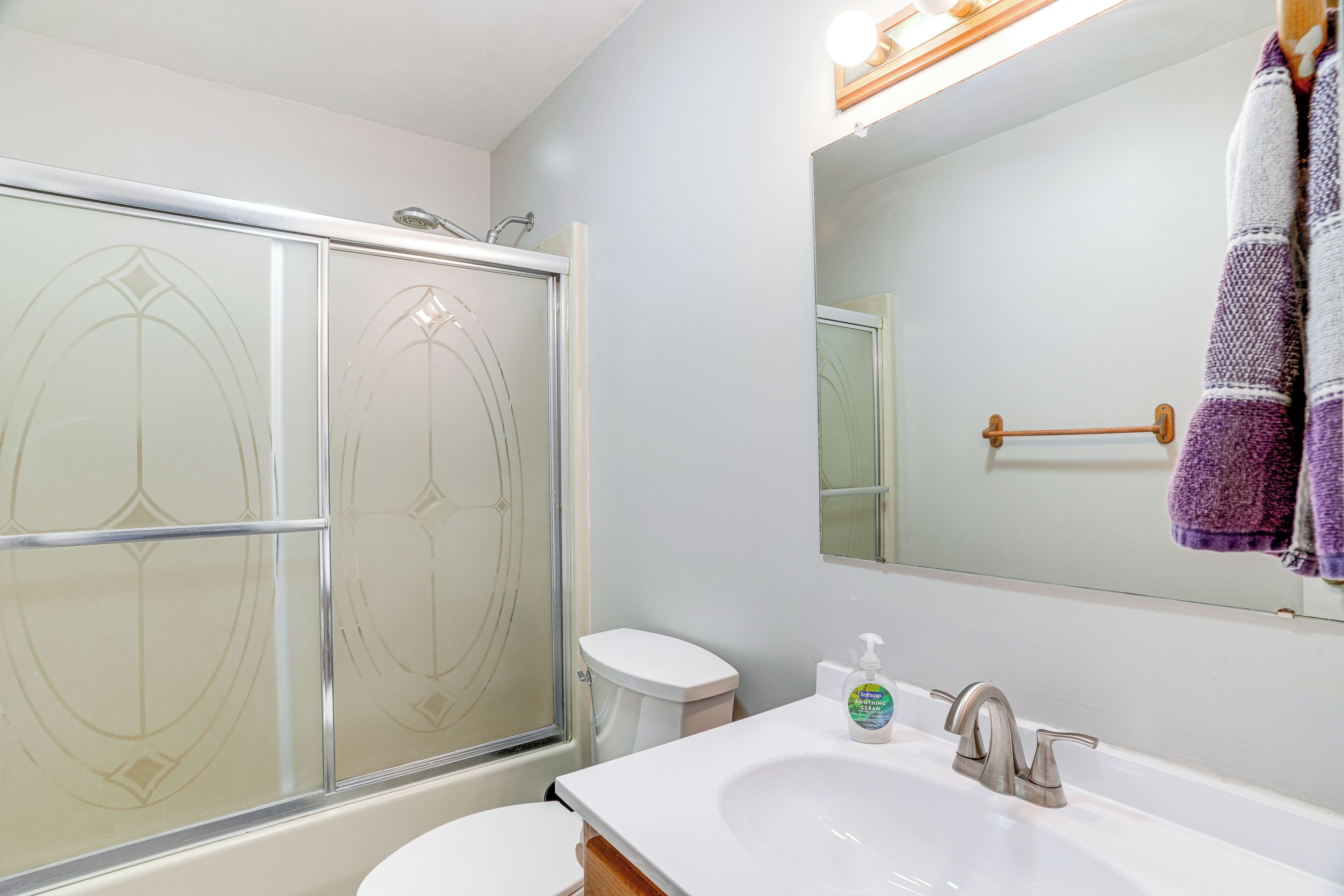 Une salle de bain avec une douche à parois de verre, un lavabo blanc doté d’un distributeur de savon et un miroir au-dessus du lavabo.