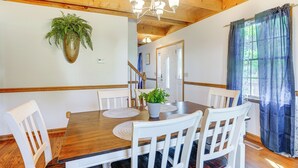 A dining area with a wooden table, white chairs, a potted plant, and a chandelier. - Mcgaheysville Home w/ Screened Porch & Gas Grill! (McGaheysville)