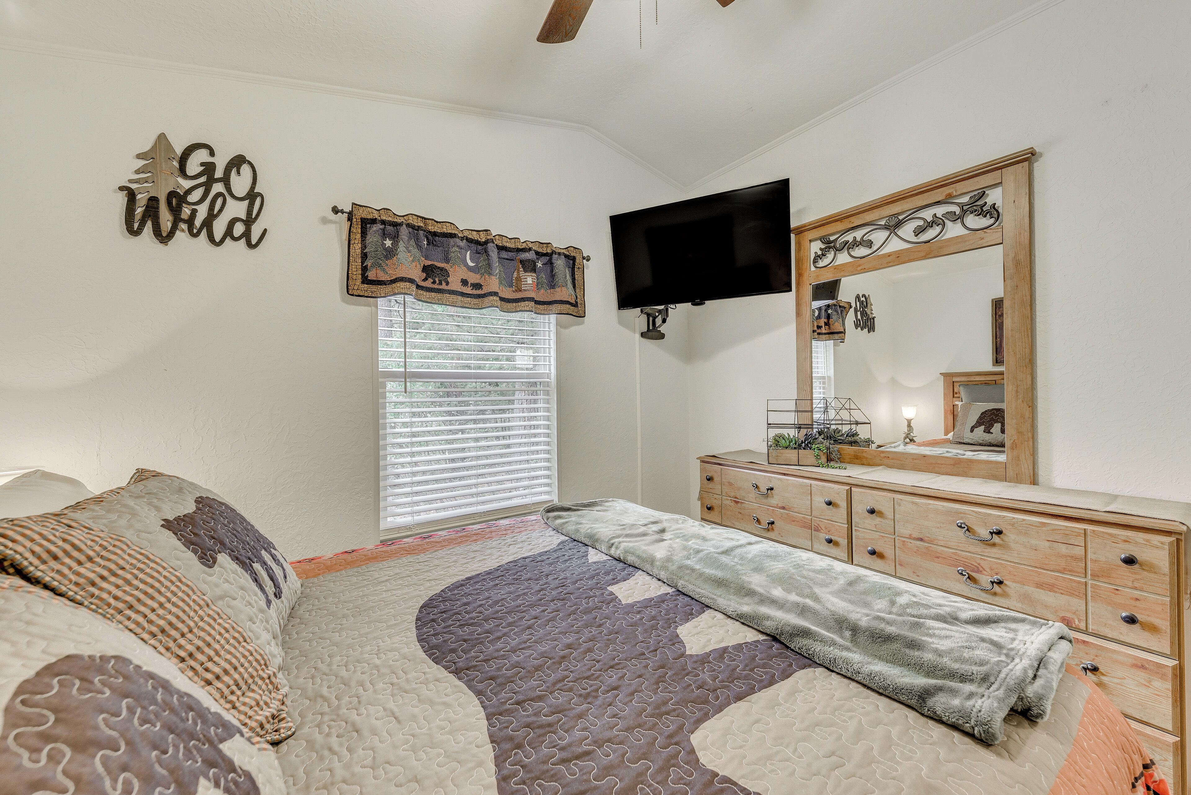 A bedroom with a bed, a dresser, a TV, and a window with blinds.